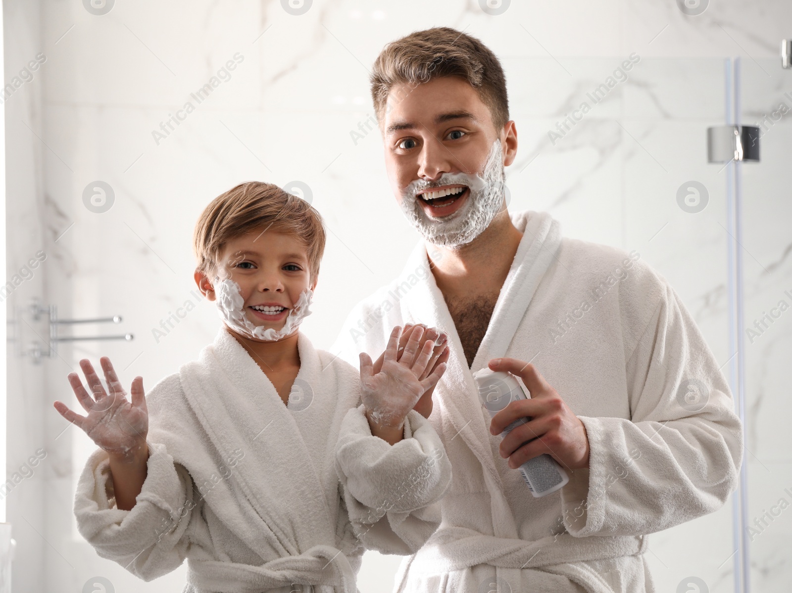 Photo of Dad and son with shaving foam on their faces having fun in bathroom