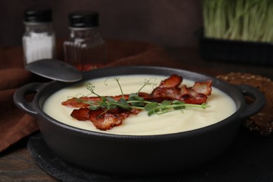 Photo of Delicious potato soup with bacon and microgreens in bowl served on wooden table, closeup