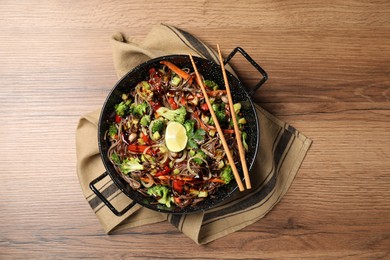 Stir-fry. Tasty noodles with meat in wok and chopsticks on wooden table, top view