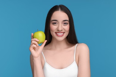 Beautiful young woman with apple on light blue background