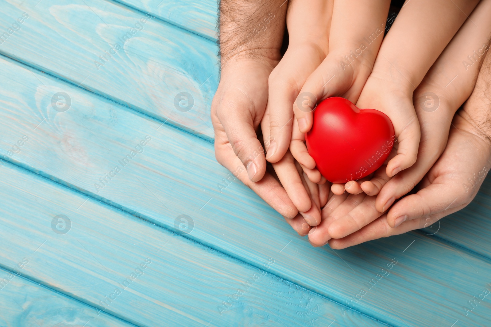 Photo of Parents and kid holding red heart in hands at light blue wooden table, top view. Space for text