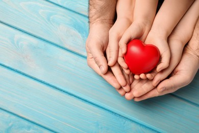Photo of Parents and kid holding red heart in hands at light blue wooden table, top view. Space for text