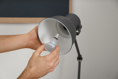 Man changing light bulb in desk lamp indoors, closeup