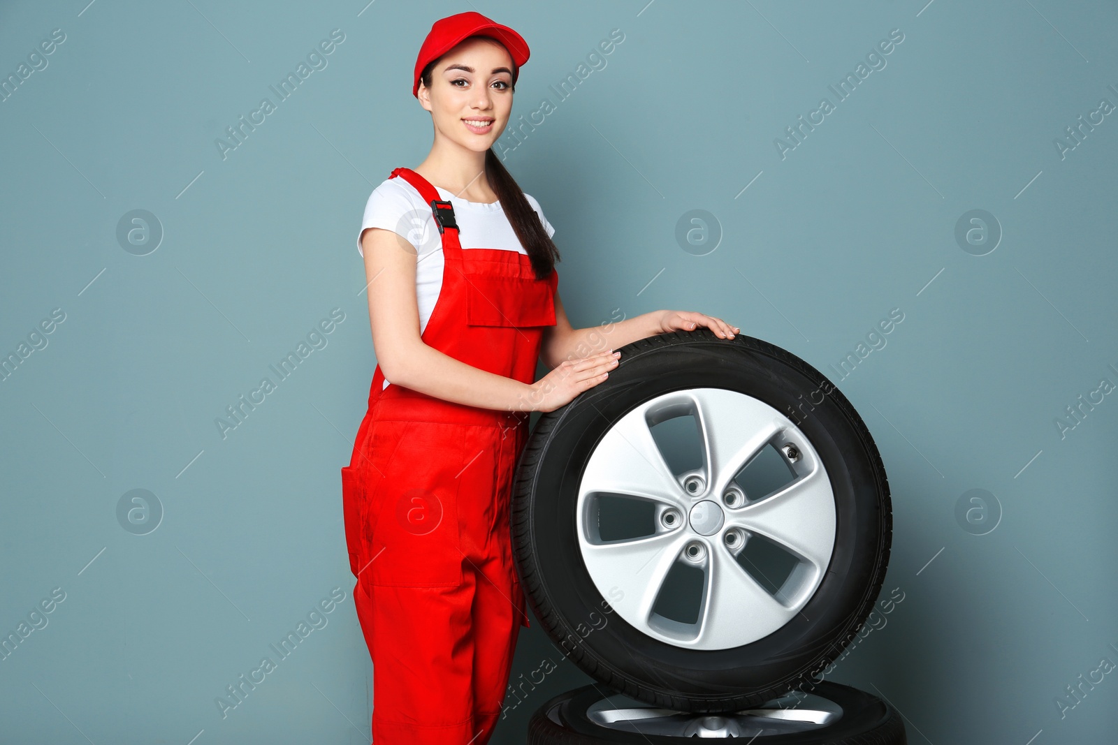 Photo of Female mechanic in uniform with car tires on color background