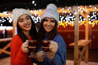 Friends with glass cups of mulled wine at winter fair. Space for text