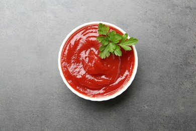 Photo of Delicious tomato ketchup and parsley in bowl on grey textured table, top view