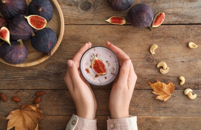 Photo of Woman with delicious fig smoothie at wooden table, top view