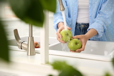 Woman washing fresh green apples in kitchen sink, closeup