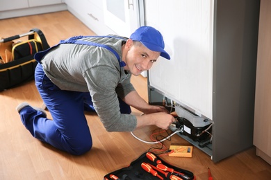 Photo of Male technician in uniform repairing refrigerator indoors