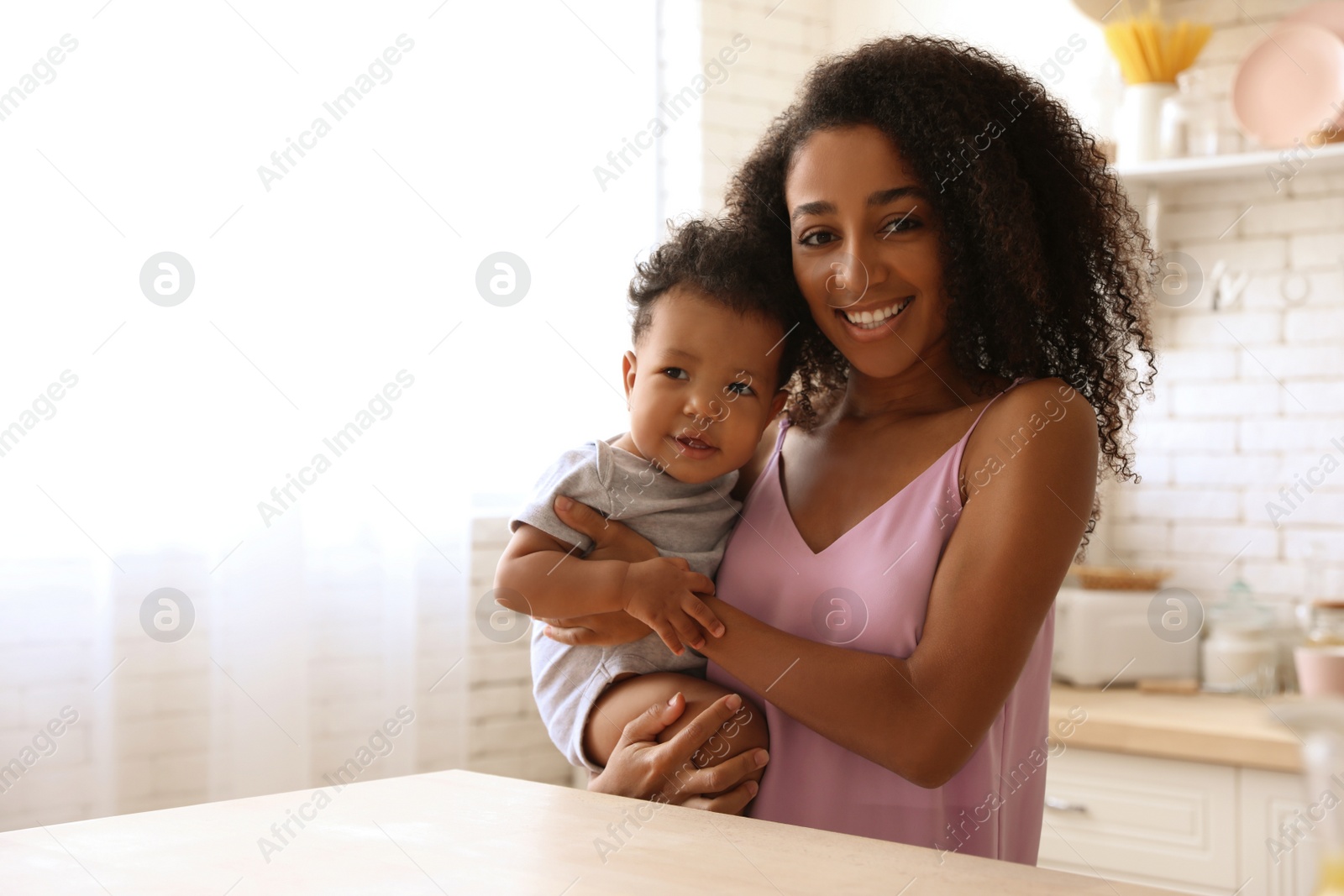 Photo of African-American woman with her baby in kitchen. Happiness of motherhood