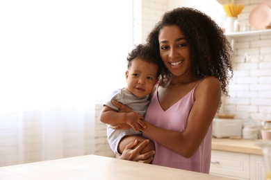 Photo of African-American woman with her baby in kitchen. Happiness of motherhood