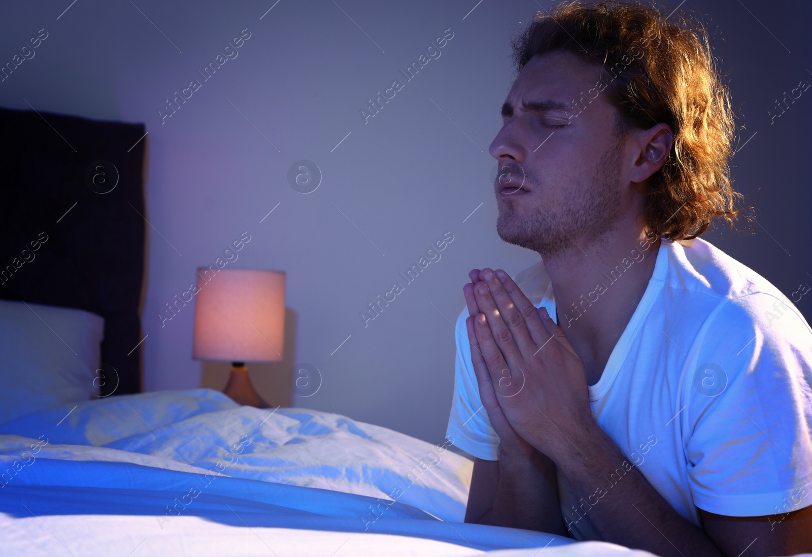 Photo of Handsome young man saying bedtime prayer in dark room at night