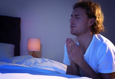 Photo of Handsome young man saying bedtime prayer in dark room at night