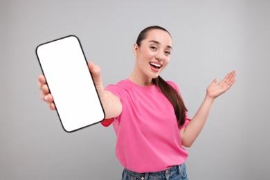Photo of Surprised woman showing smartphone in hand on light grey background