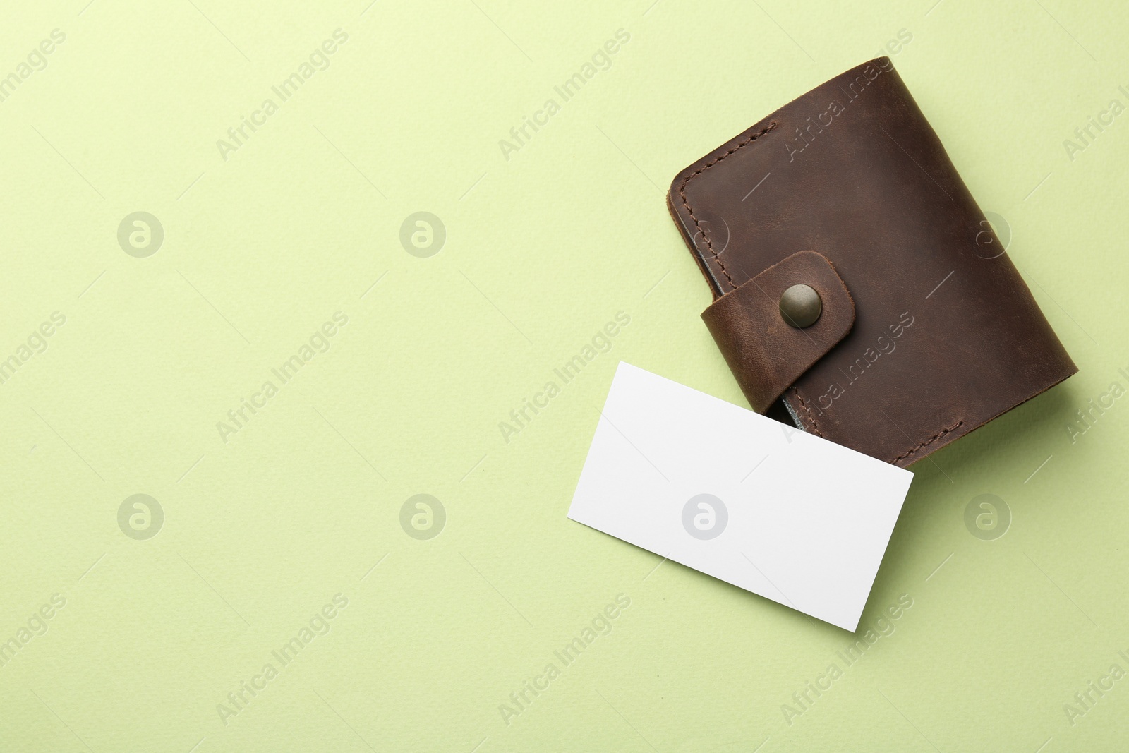 Photo of Leather business card holder with blank card on light green background, top view. Space for text