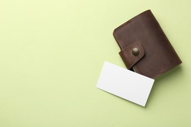 Photo of Leather business card holder with blank card on light green background, top view. Space for text