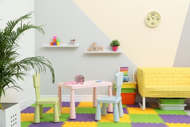 Photo of Stylish playroom interior with table, chairs and sofa