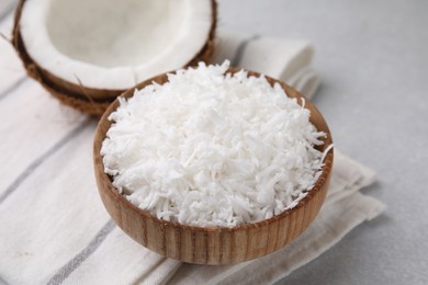 Photo of Coconut flakes in bowl and nut on light grey table, closeup