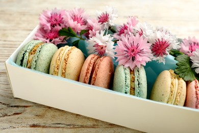 Photo of Delicious macarons and flowers in box on white wooden table