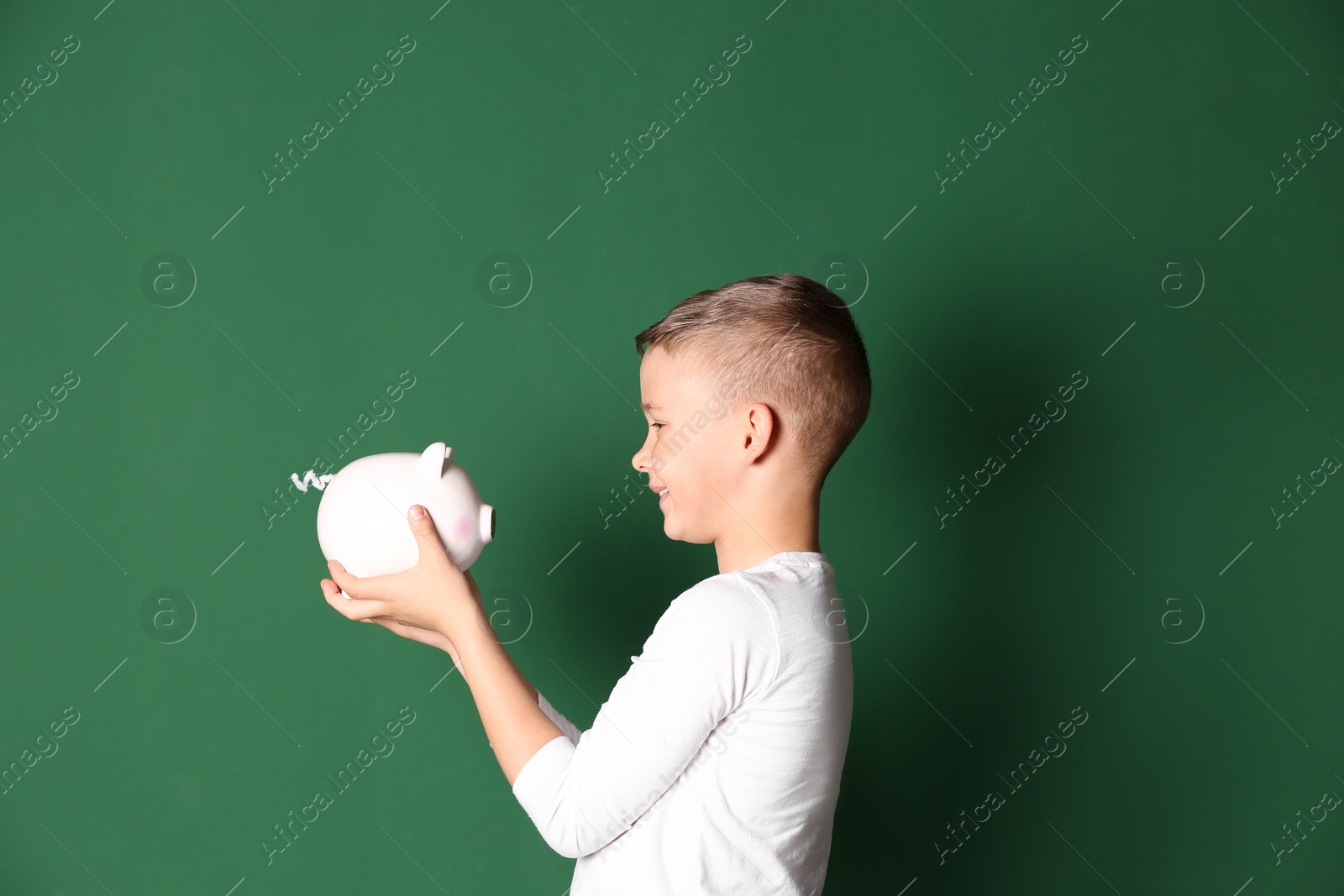 Photo of Little boy with piggy bank on color background