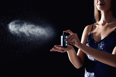 Young woman spraying perfume on black background, closeup