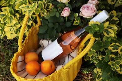 Photo of Yellow wicker bag with roses, peaches and wine outdoors, above view