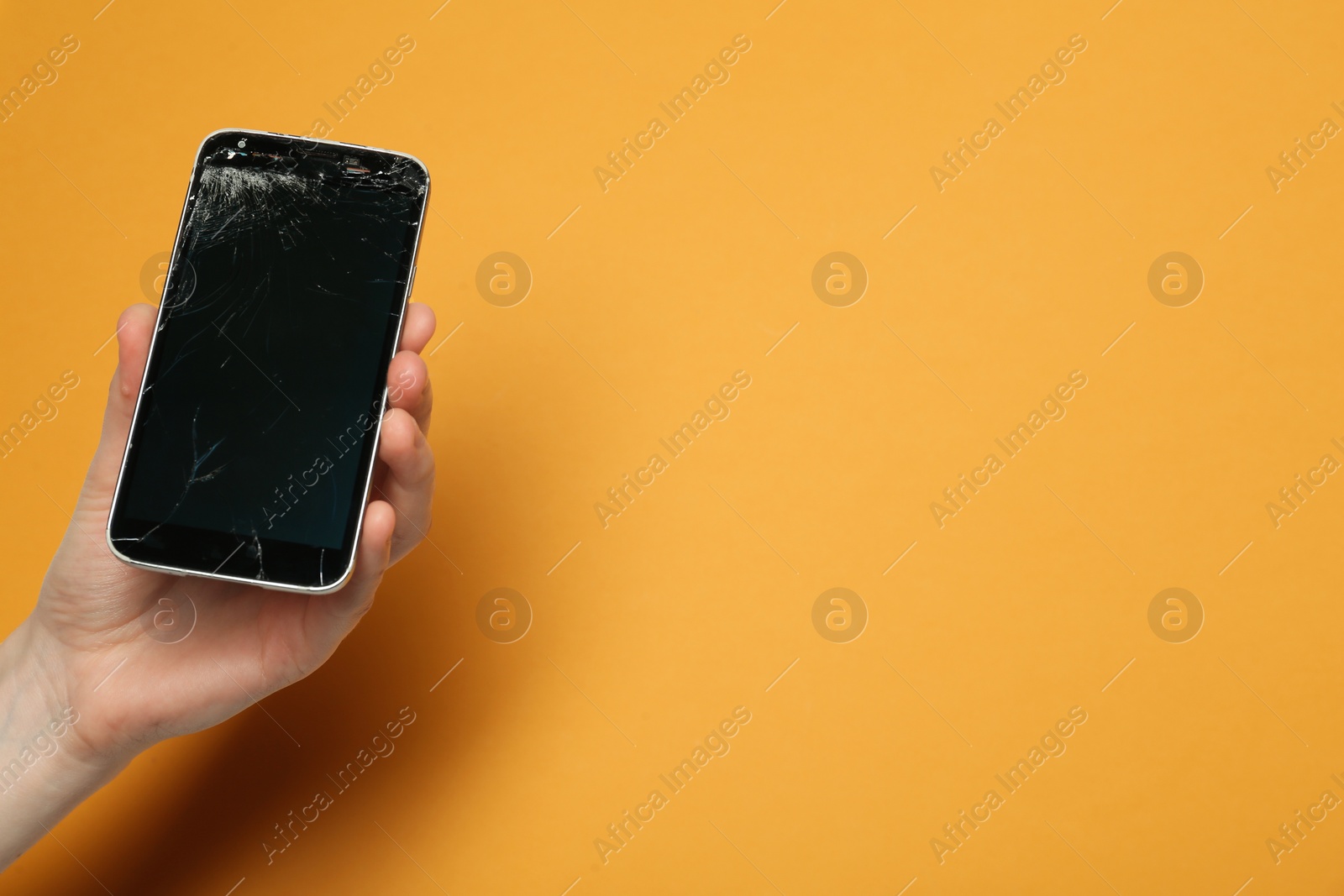 Photo of Woman holding damaged smartphone on orange background, closeup with space for text. Device repairing