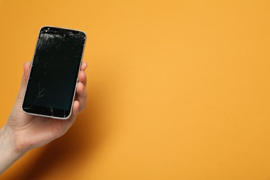 Photo of Woman holding damaged smartphone on orange background, closeup with space for text. Device repairing