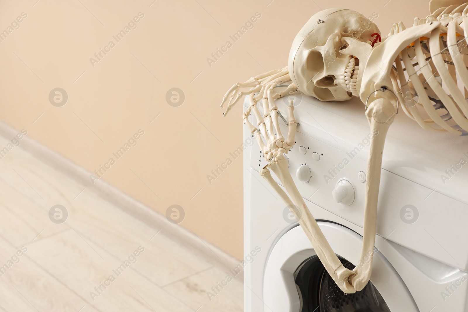 Photo of Waiting concept. Human skeleton lying on washing machine near beige wall indoors, space for text