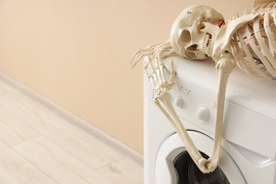 Photo of Waiting concept. Human skeleton lying on washing machine near beige wall indoors, space for text