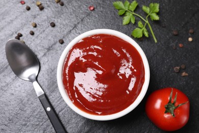 Photo of Organic ketchup in bowl, fresh tomato and spices on black table, flat lay. Tomato sauce