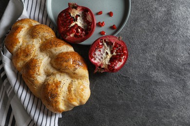 Photo of Homemade braided bread and pomegranate on grey table, flat lay with space for text. Cooking traditional Shabbat challah