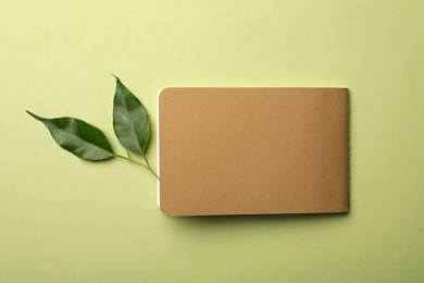 Photo of Kraft planner and leaves on light green background, flat lay