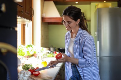Photo of Young woman cutting fresh tomatoes at countertop in kitchen