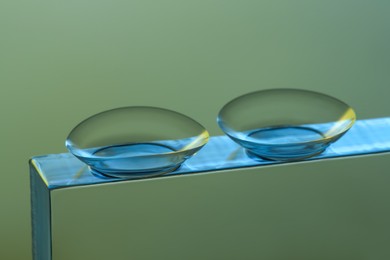 Pair of contact lenses on glass against grey background, closeup