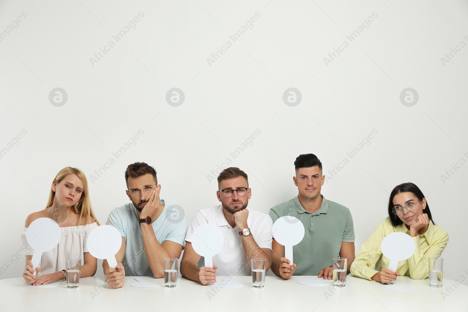 Photo of Panel of disappointed judges holding blank score signs at table on white background. Space for text