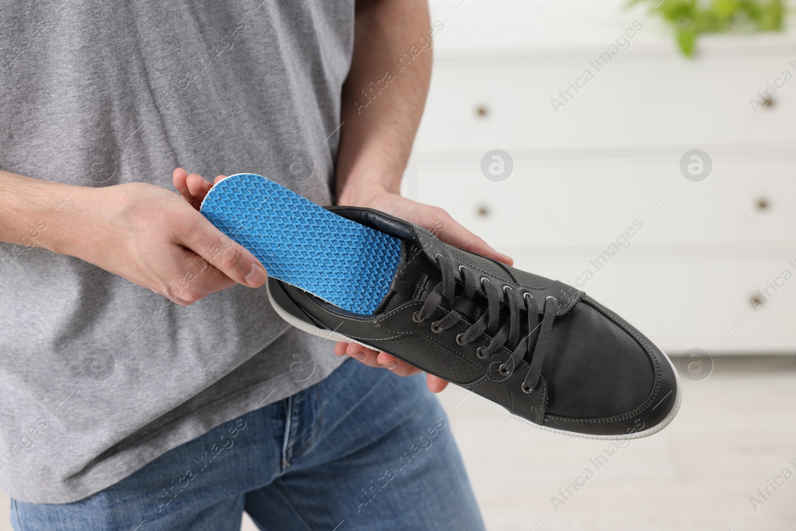 Photo of Man putting orthopedic insole into shoe indoors, closeup