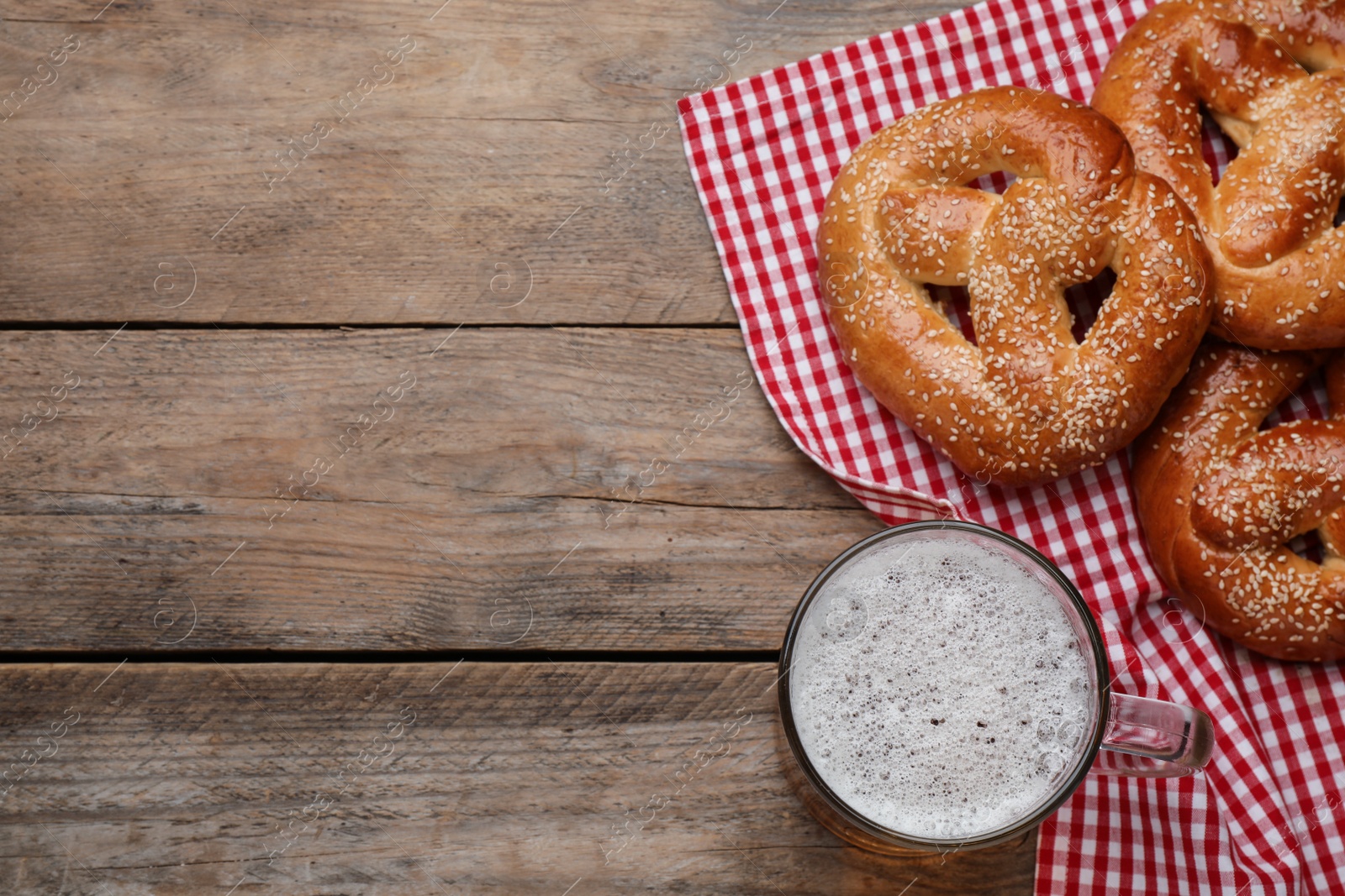 Photo of Tasty pretzels and glass of beer on wooden table, flat lay. Space for text