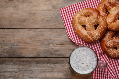 Photo of Tasty pretzels and glass of beer on wooden table, flat lay. Space for text