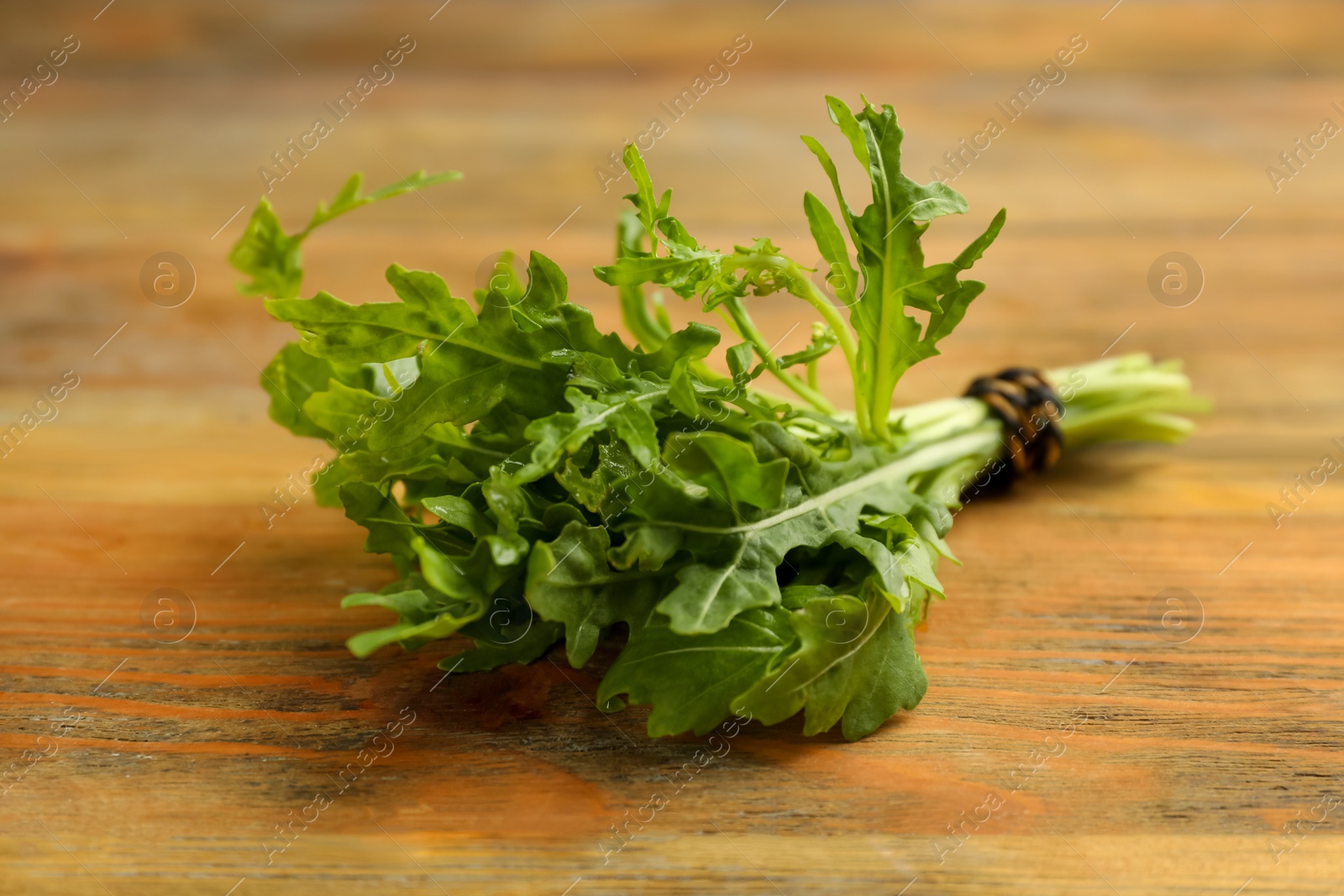 Photo of Bunch of fresh arugula on wooden table, closeup