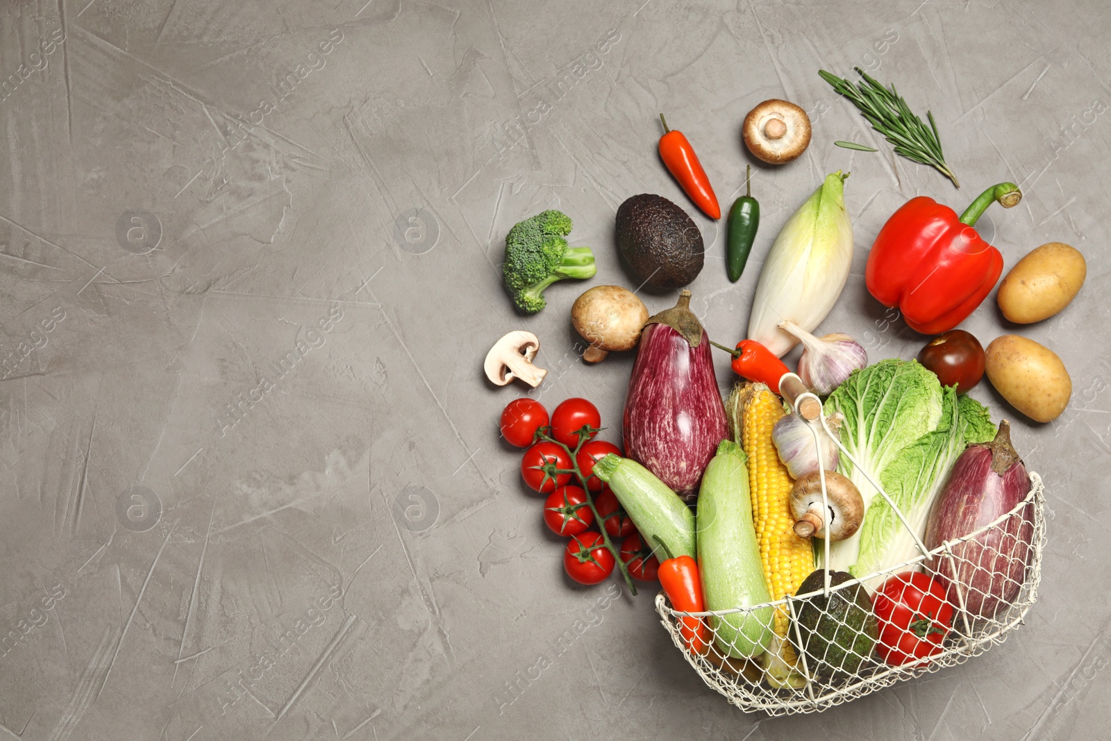 Photo of Different vegetables and metal basket on grey background, top view. Space for text