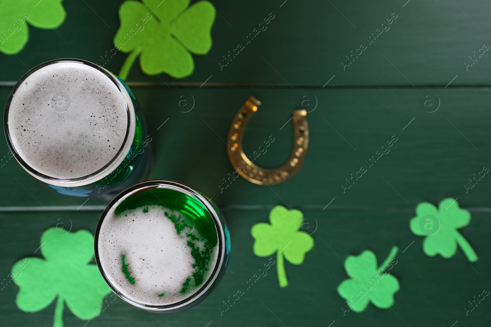 Photo of St. Patrick's day party. Green beer, horseshoe and decorative clover leaves on wooden table, flat lay. Space for text