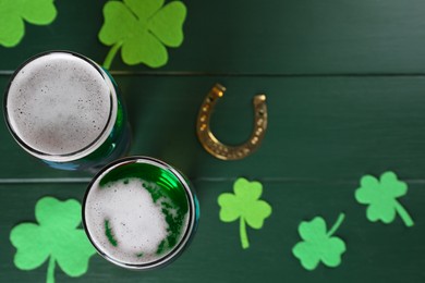 Photo of St. Patrick's day party. Green beer, horseshoe and decorative clover leaves on wooden table, flat lay. Space for text