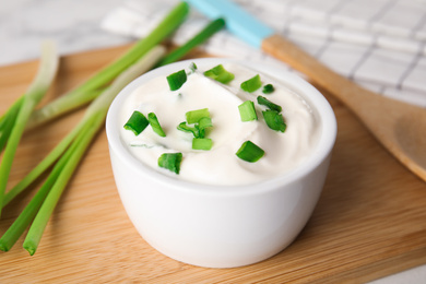 Photo of Fresh sour cream with onion on wooden board, closeup