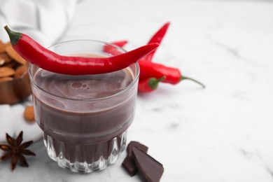 Glass of hot chocolate with chili pepper on white marble table, closeup. Space for text