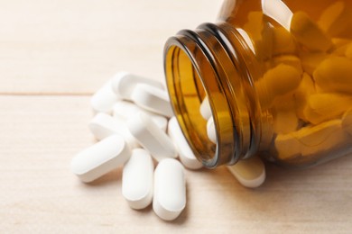 Photo of Bottle and vitamin pills on wooden table, closeup