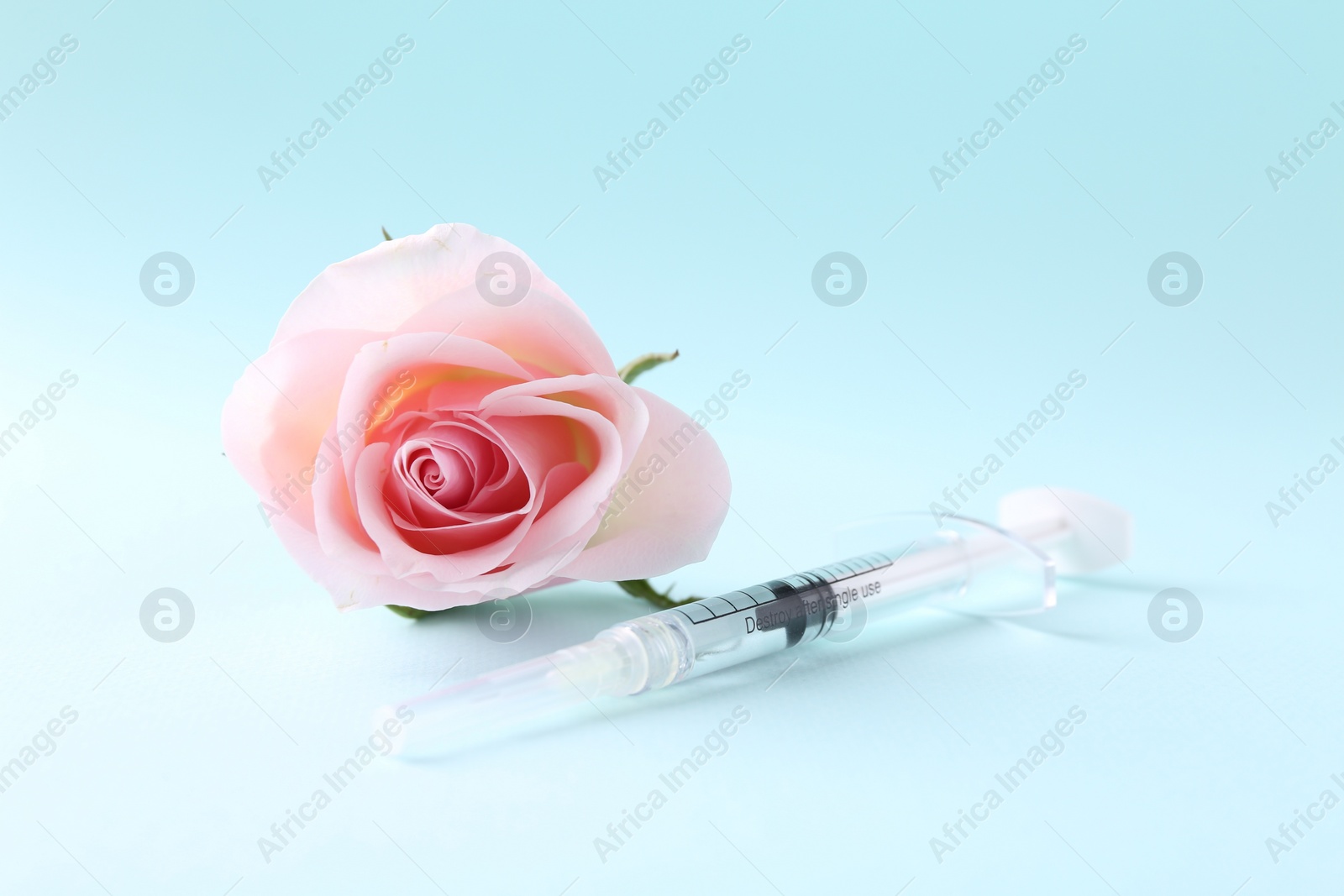 Photo of Cosmetology. Medical syringe and rose flower on light blue background