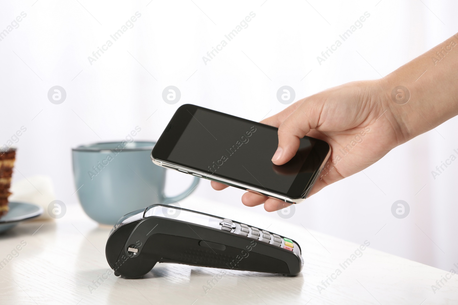 Photo of Woman using terminal for contactless payment with smartphone in cafe