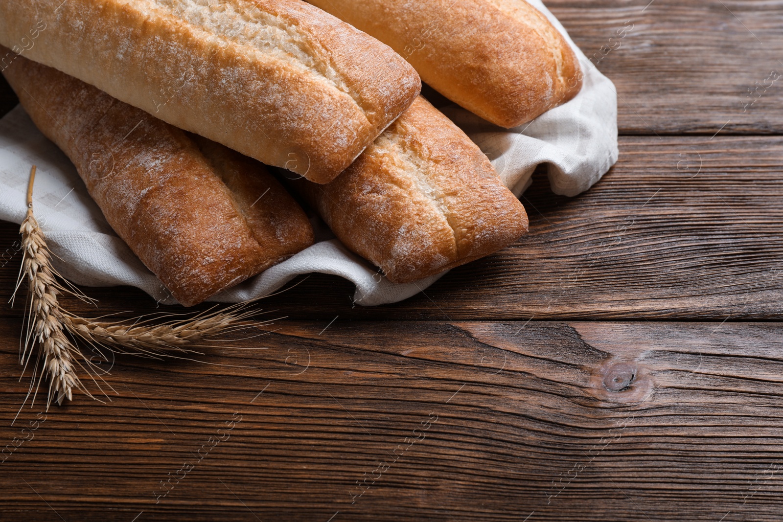 Photo of Different tasty baguettes and spikelets on wooden table, closeup