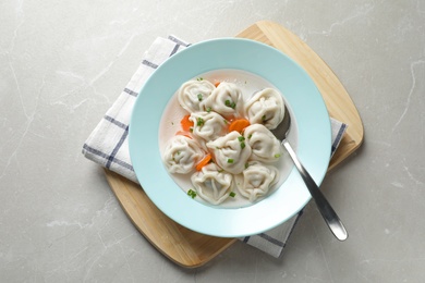 Board with plate of dumplings on grey marble table, top view